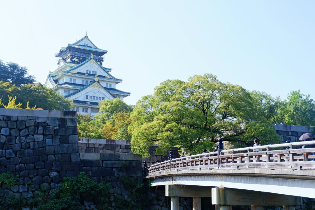 white concrete bridge over green trees during daytime. Osaka Castle