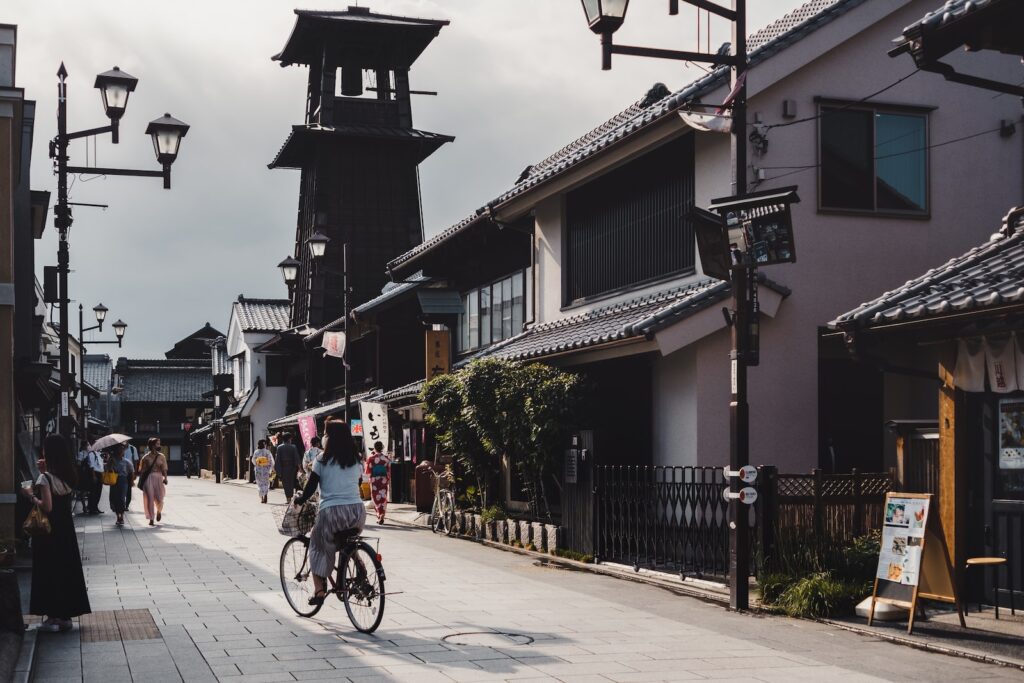 people riding bicycles on road near buildings during daytime. Saitama Cover Photo